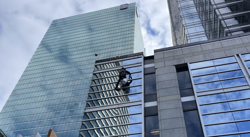 Professional window cleaners using a boatswain chair to clean windows with the RBC building in the backdrop