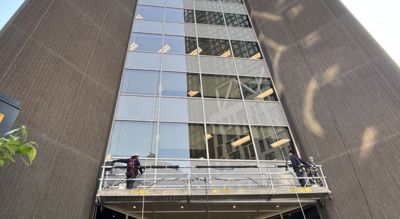 Stage system being used to clean the windows of a tall building, with workers carefully washing the exterior
