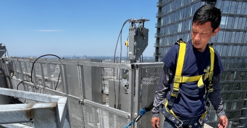 Employee safely secured to a swing stage, ready to begin high-rise window cleaning on a commercial building